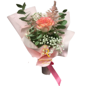 Ramo de una rosa rosada con follaje verde y flores blancas, envuelto en papel rosado